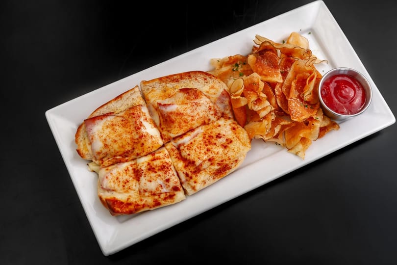 Four cheesy sandwiches with paprika, served with crispy chips and a side of ketchup.