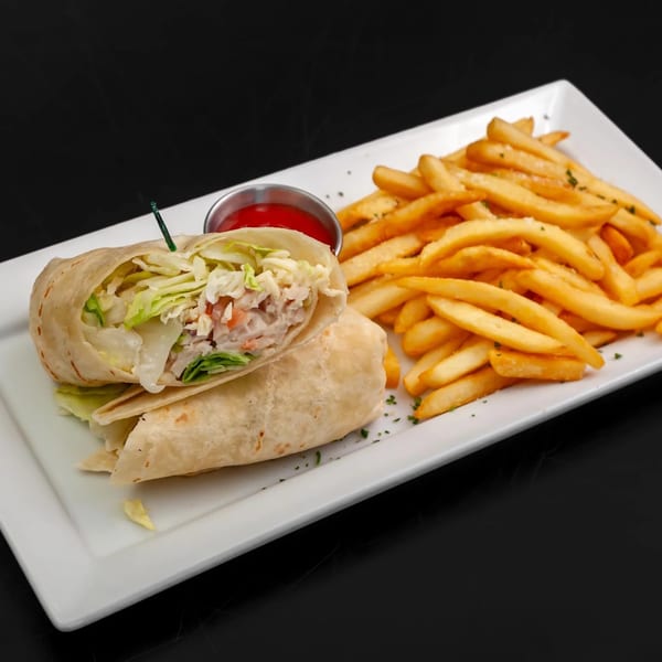 A chicken Caesar wrap, cut in half, with a side of golden french fries and ketchup.