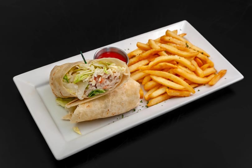 A chicken Caesar wrap, cut in half, with a side of golden french fries and ketchup.